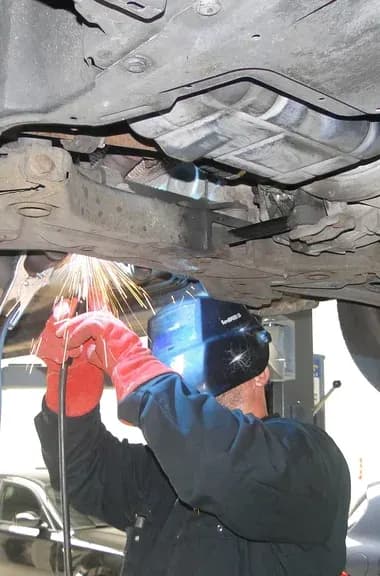 Monteur aan het werk aan de onderkant van een auto op de brug bij Prima Auto's in Nijverdal